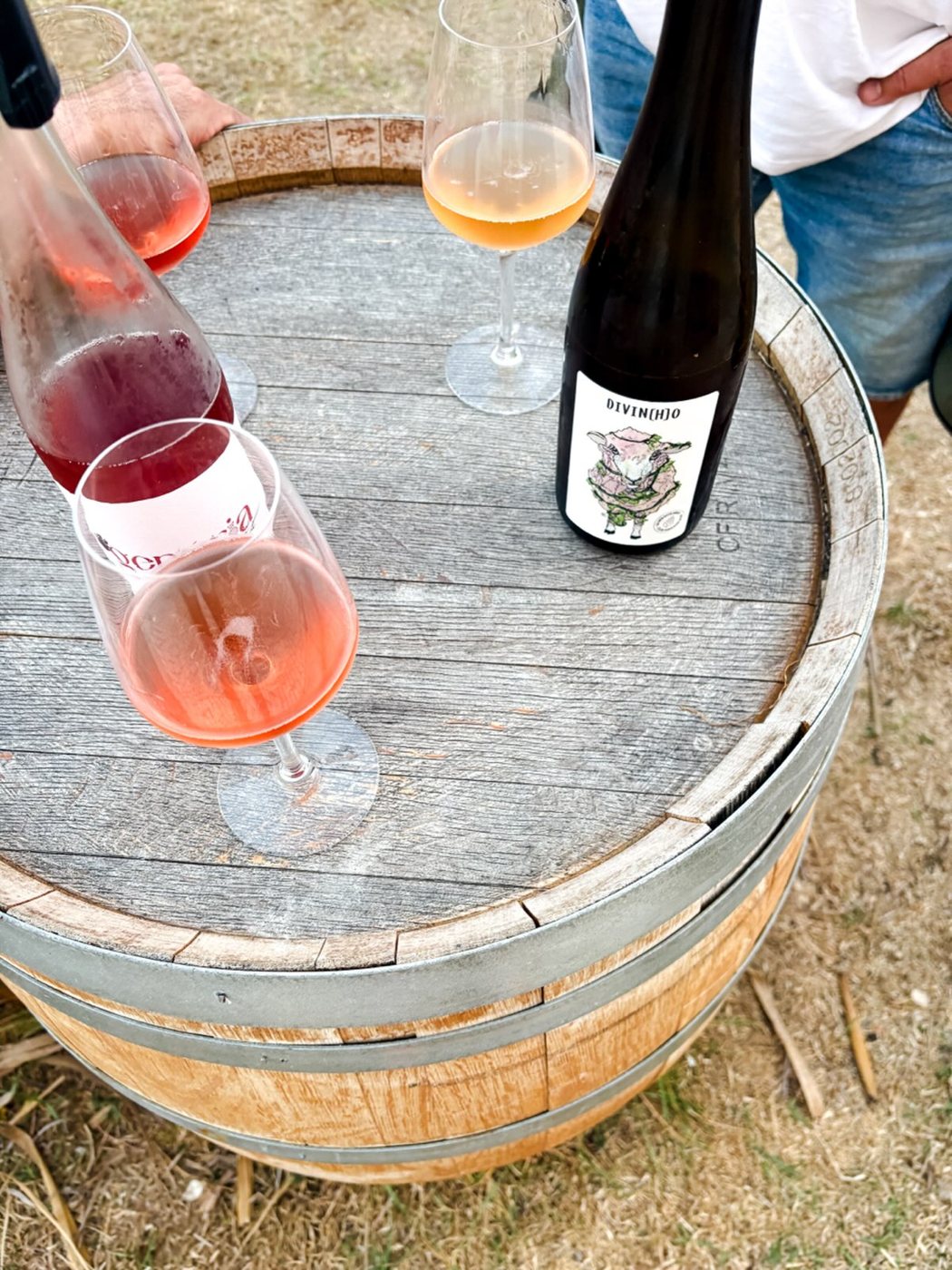 Copos de rosé e vinho laranja com uma garrafa sobre um barril, ao ar livre